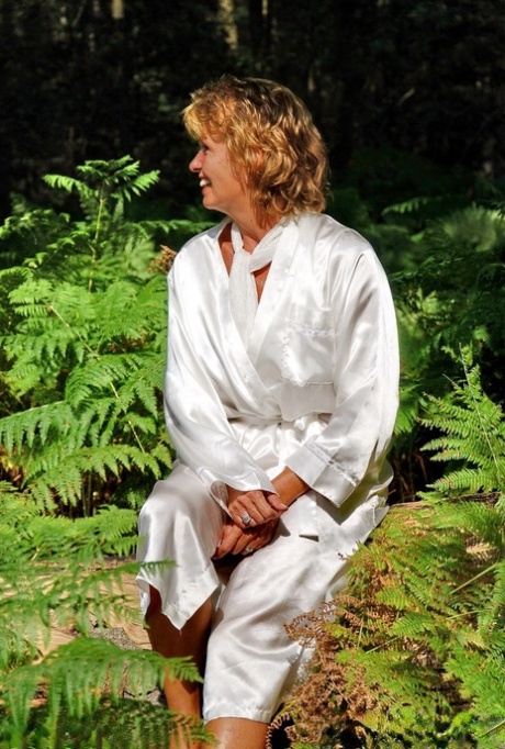 Older redhead removes a robe to stand naked in red heels while in the woods