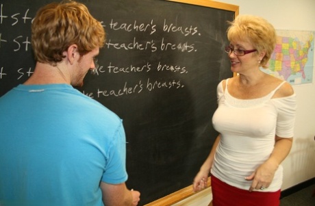 Mature teacher Tracy Lick jerks on a student's huge dick in the classroom
